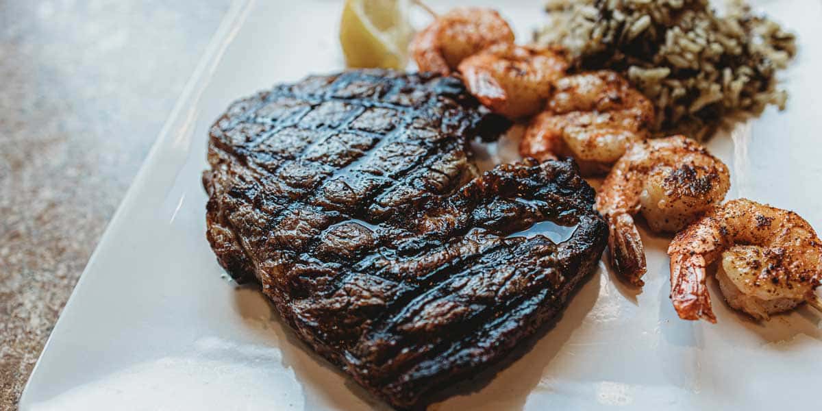A photo of a ribeye steak, shrimp and rice